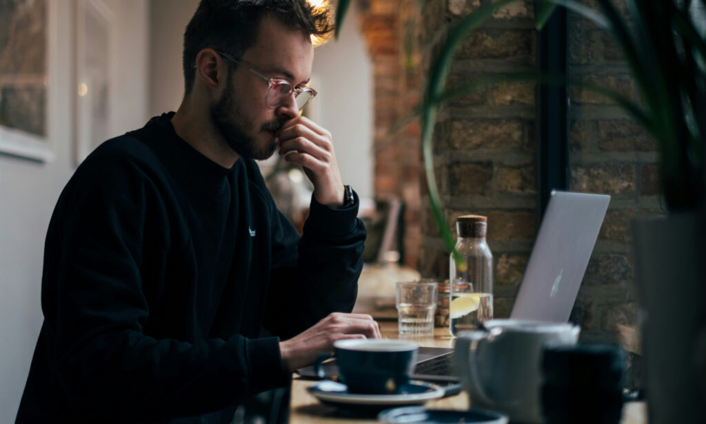 Man working on a laptop in a cafe, representing contractors handling IRS information and complying with IRS Publication 4812 media protection and data wiping standards.