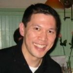 Smiling portrait of Ryan Yee, guest writer for Jetico, wearing a black shirt in a warmly lit setting